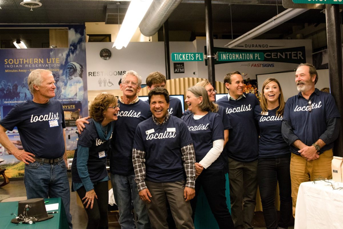 A candid photo of eight people standing in a row all wearing t-shirts that read "Localist".