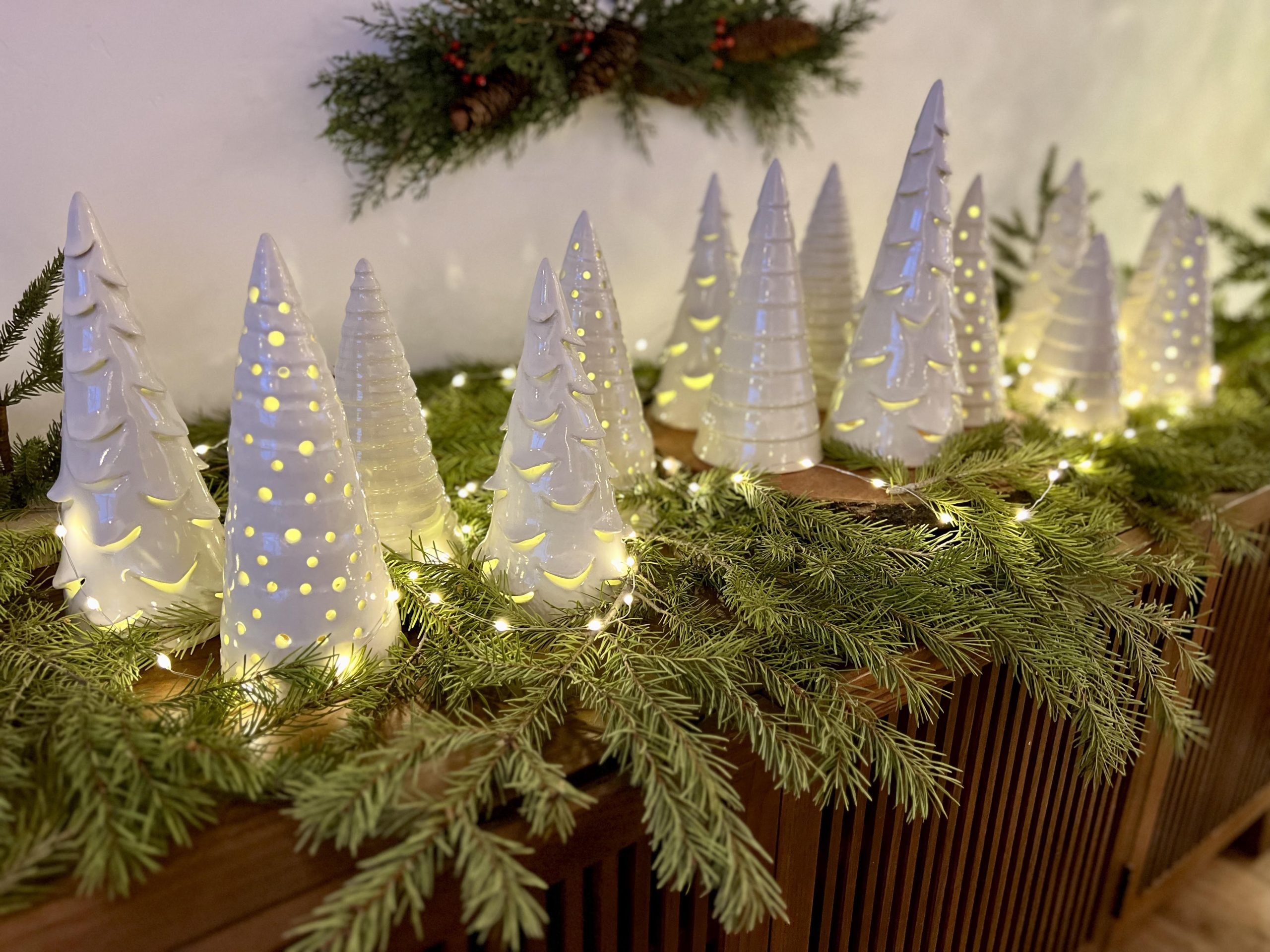 White ceramic Christmas trees surrounded by garland.