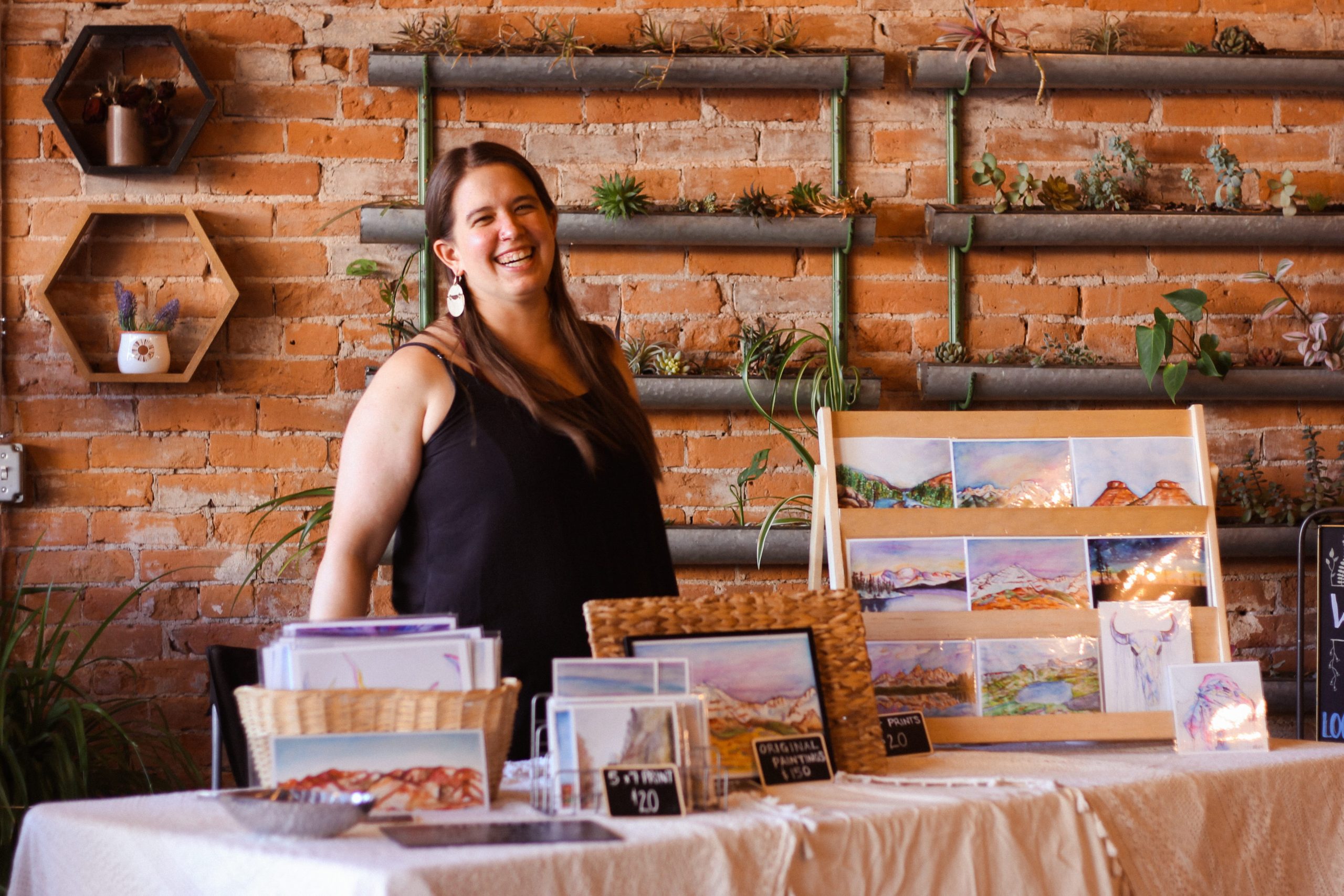 Artists standing at a table with works displayed in front of her.