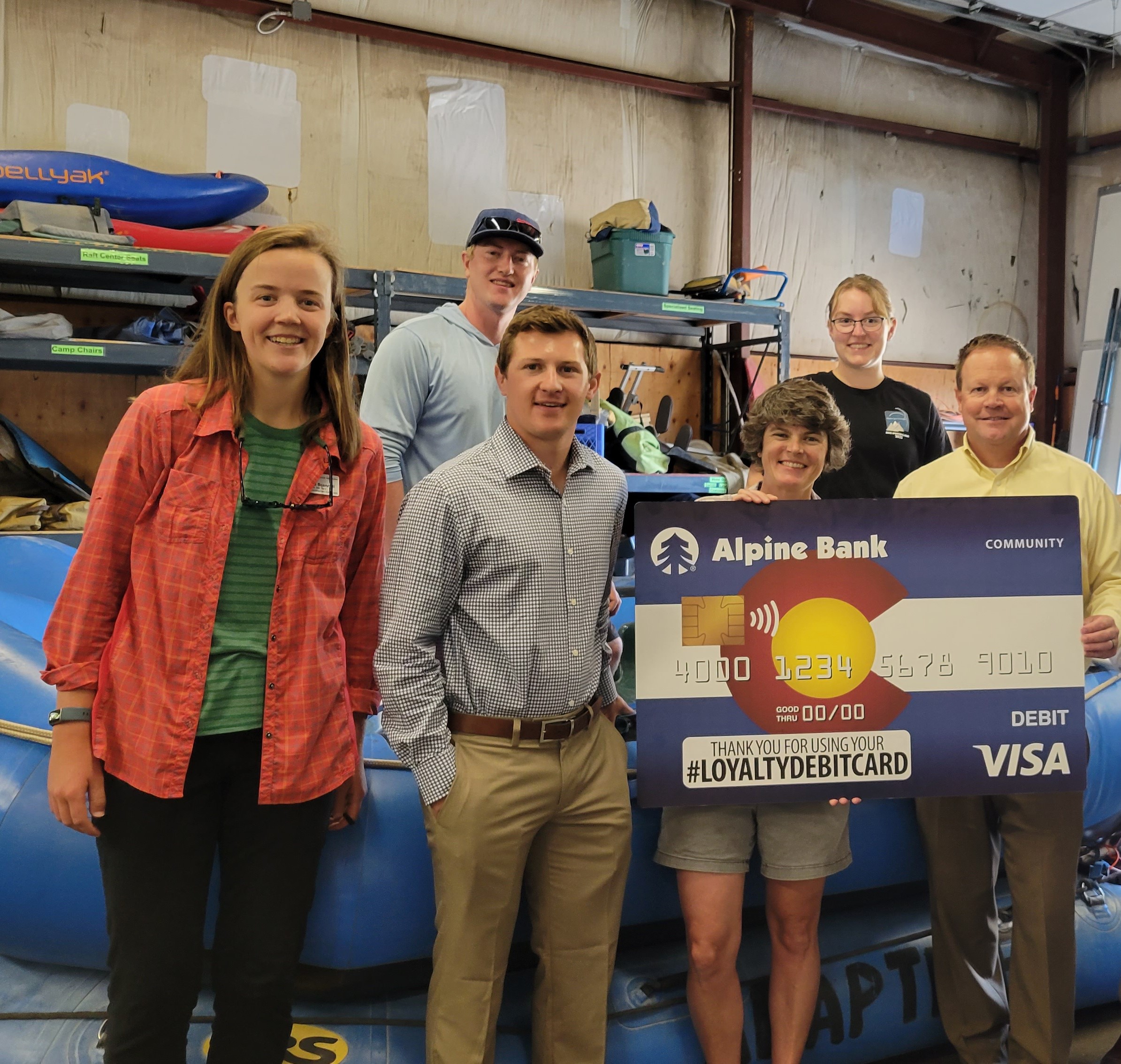 Six people in a photo with one holding a large Alpine Bank Credit Card posterboard.