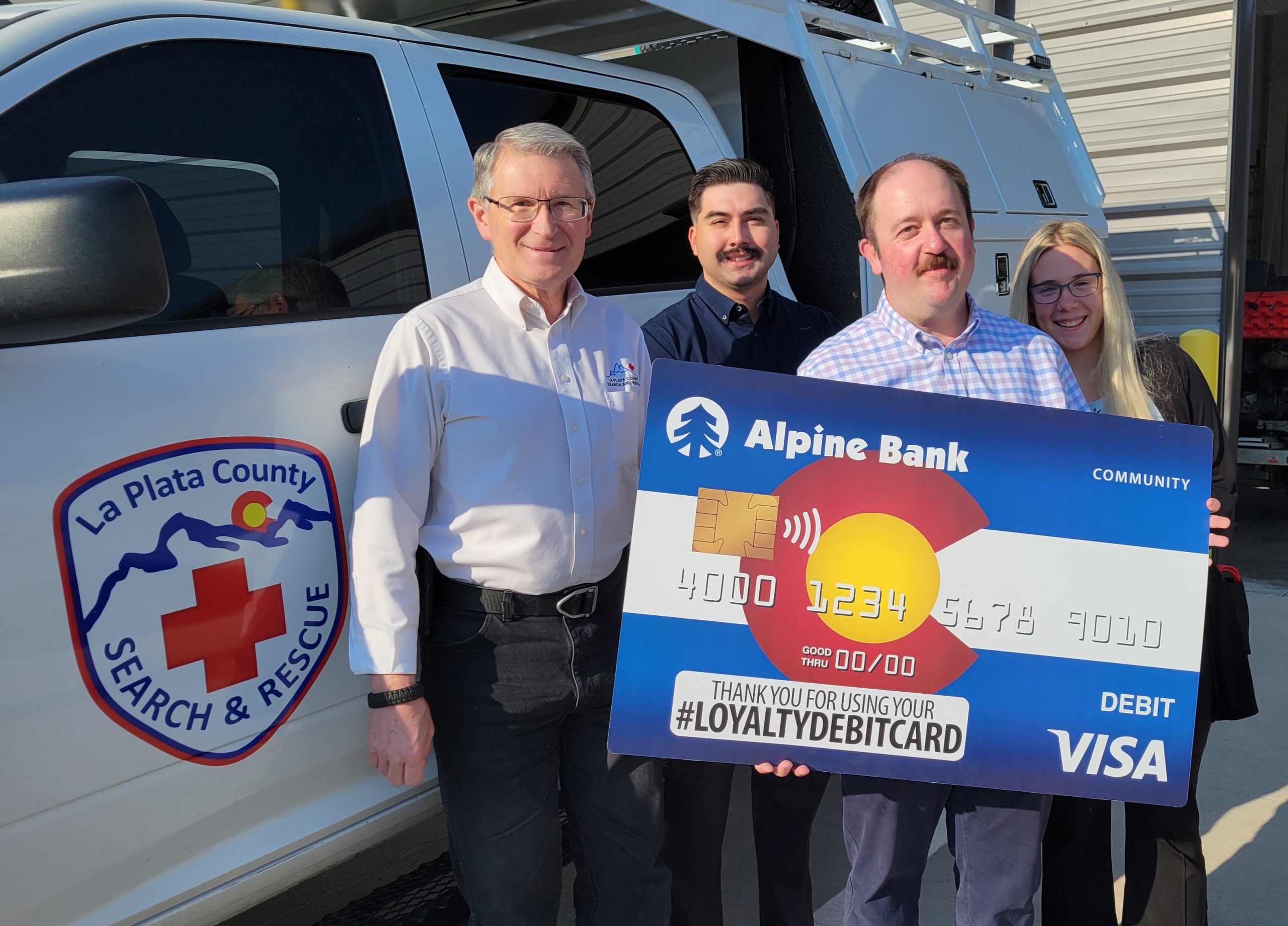 Four people holding a large posterboard of an Alpine Bank credit card.