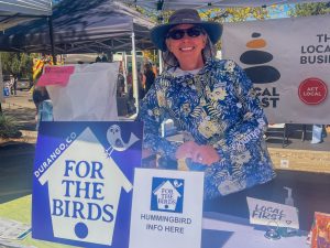 For the Birds Durango A woman leaning against a large bag of bird feed under a tent.