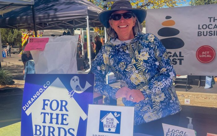 A woman leaning against a large bag of bird feed under a tent.