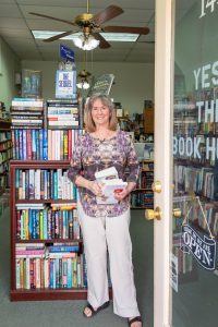 Indie-Booksellers-Day-22 A photo of a woman standing a a bookstore doorway holding a stack of books.