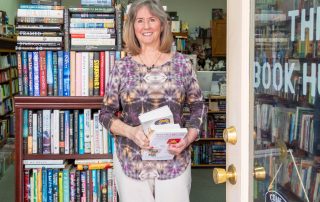 A photo of a woman standing a a bookstore doorway holding a stack of books.