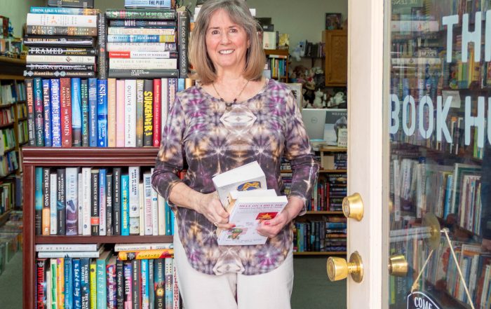 A photo of a woman standing a a bookstore doorway holding a stack of books.