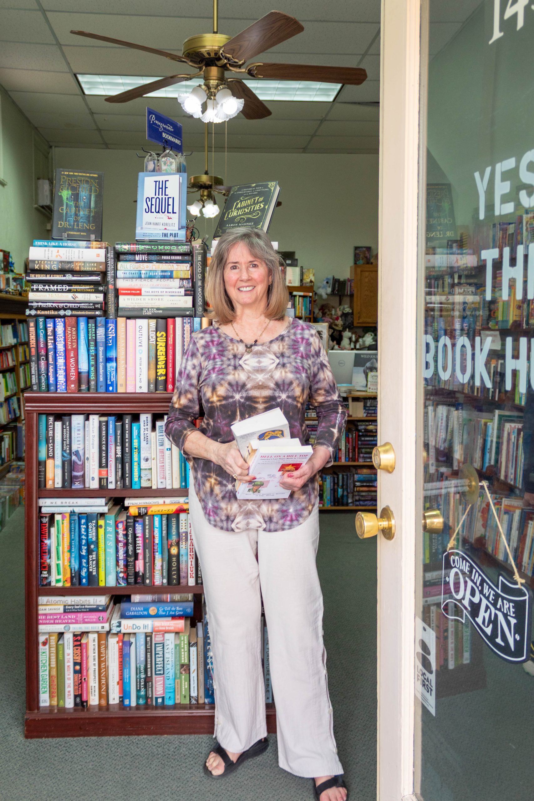 A photo of a woman standing a a bookstore doorway holding a stack of books.